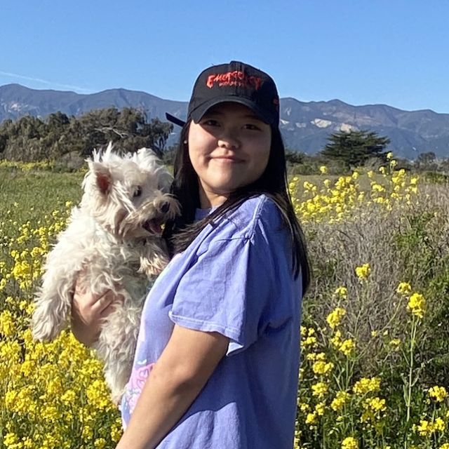 Photo of Zoe Chang standing in front of mustard flowers holding her dog.